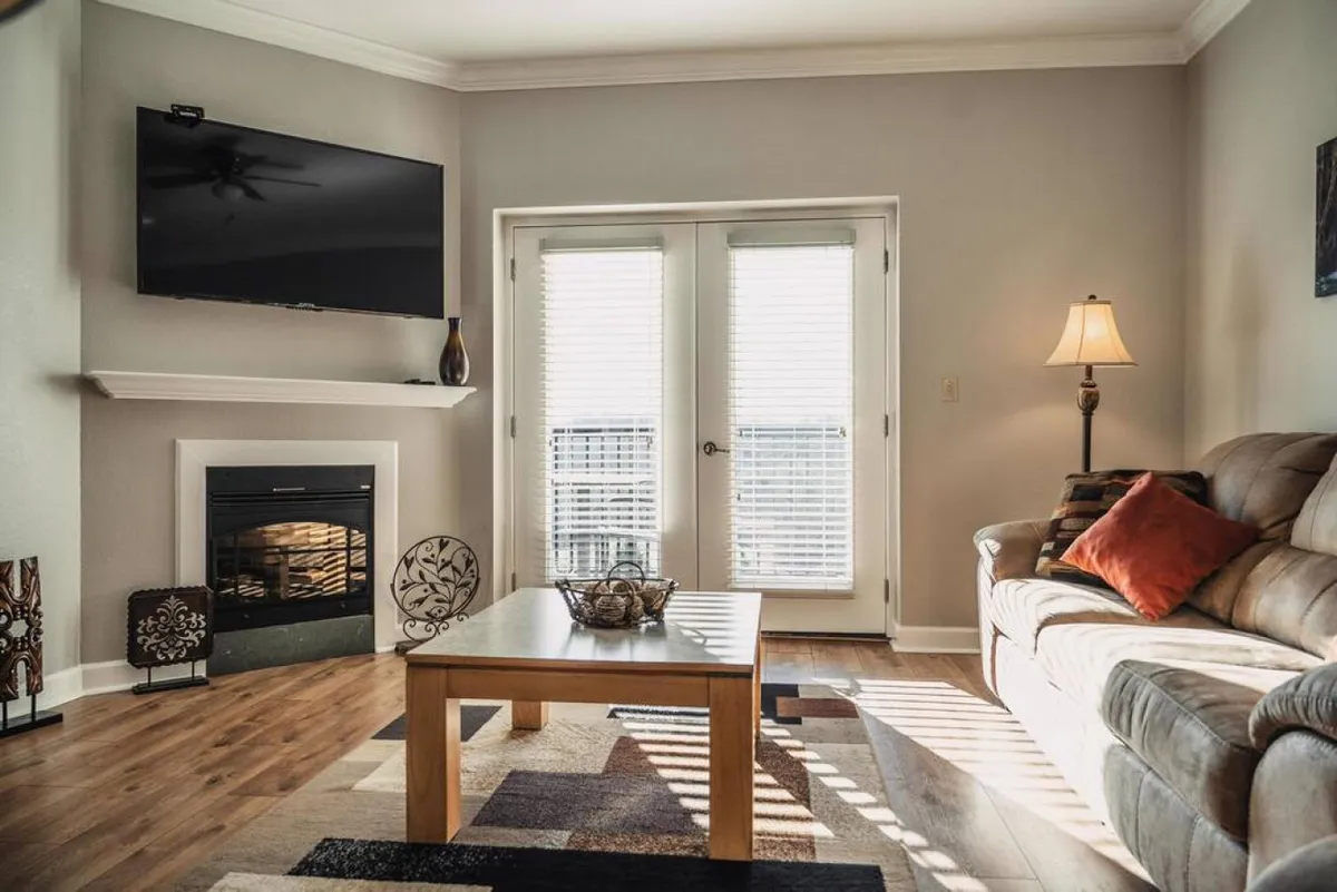 This image showcases a cozy living area with a plush sofa, a coffee table, a fireplace, a TV, and sliding doors that likely open onto a balcony. Warm lighting and inviting decor make it a perfect spot for relaxing, socializing, or enjoying a movie night with family or friends.