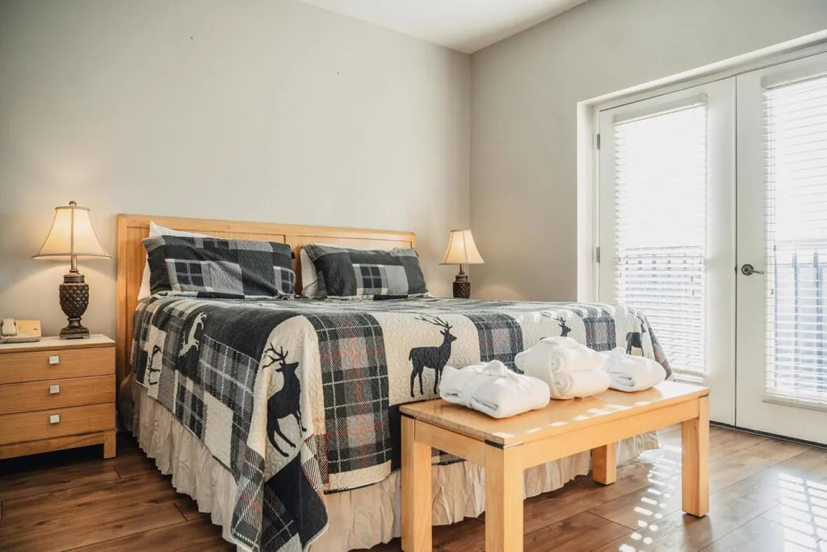 A sunlit bedroom with a plush king bed covered in a warm quilt, bedside lamps, a dressing table, and sliding doors letting in plenty of natural light. The mood is inviting and restful, perfect for relaxation after a busy day.