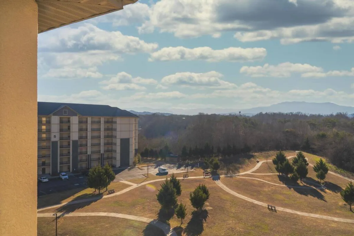 This image displays the multi-story condo building set in a park-like setting, with winding pathways weaving through green spaces and benches placed throughout. The mountains provide a scenic backdrop, creating an inviting environment for outdoor activities and group gatherings.