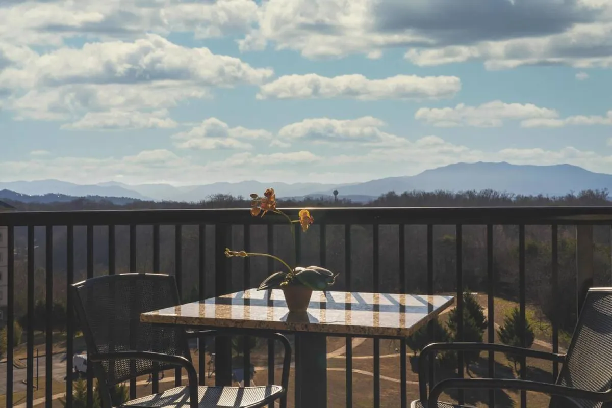 This exterior shot highlights a serene balcony table adorned with an orchid plant, overlooking expansive mountain views under a cloudy sky. The inviting outdoor setting conveys relaxation and a close connection to the Smoky Mountain landscape, perfect for enjoying a morning coffee before a day of exploration.