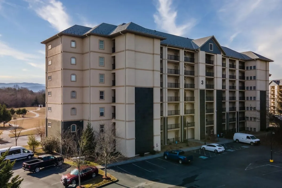 This exterior image features the property's building facade with a visible parking area and the inviting surrounding landscape. The scene captures accessibility, ample parking, and a welcoming approach to the property, hinting at convenience and ease of arrival for guests.