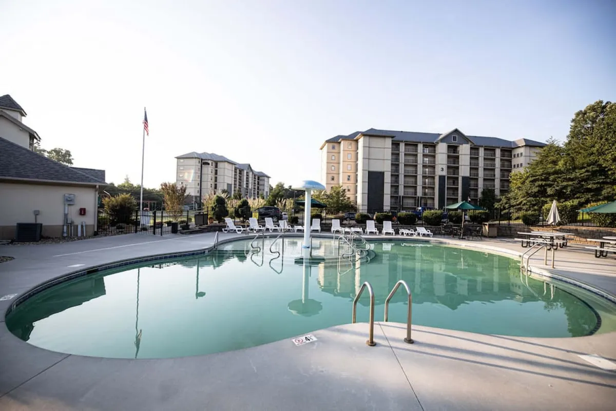 This image captures the resort's inviting outdoor swimming pool area, featuring clear blue water, a row of lounge chairs, lush greenery, and surrounding resort buildings. The setting is relaxed and open, highlighting the pool as a prime destination for warm-weather fun and social gatherings.