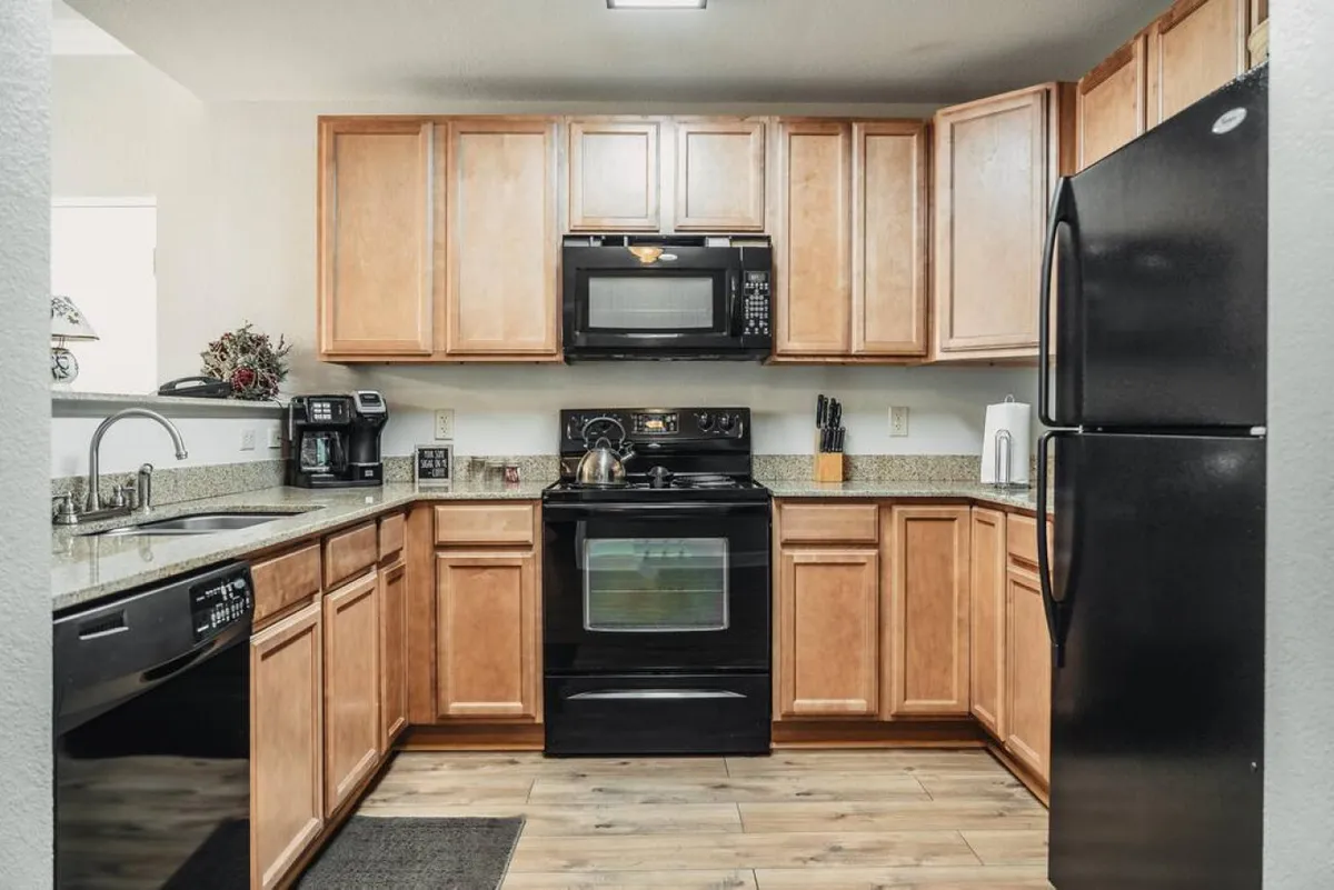 This image showcases a modern kitchen with granite countertops, black appliances, and wooden cabinets. The space is organized and ready for meal preparation, with ample counter space and a welcoming atmosphere for cooking and entertaining.