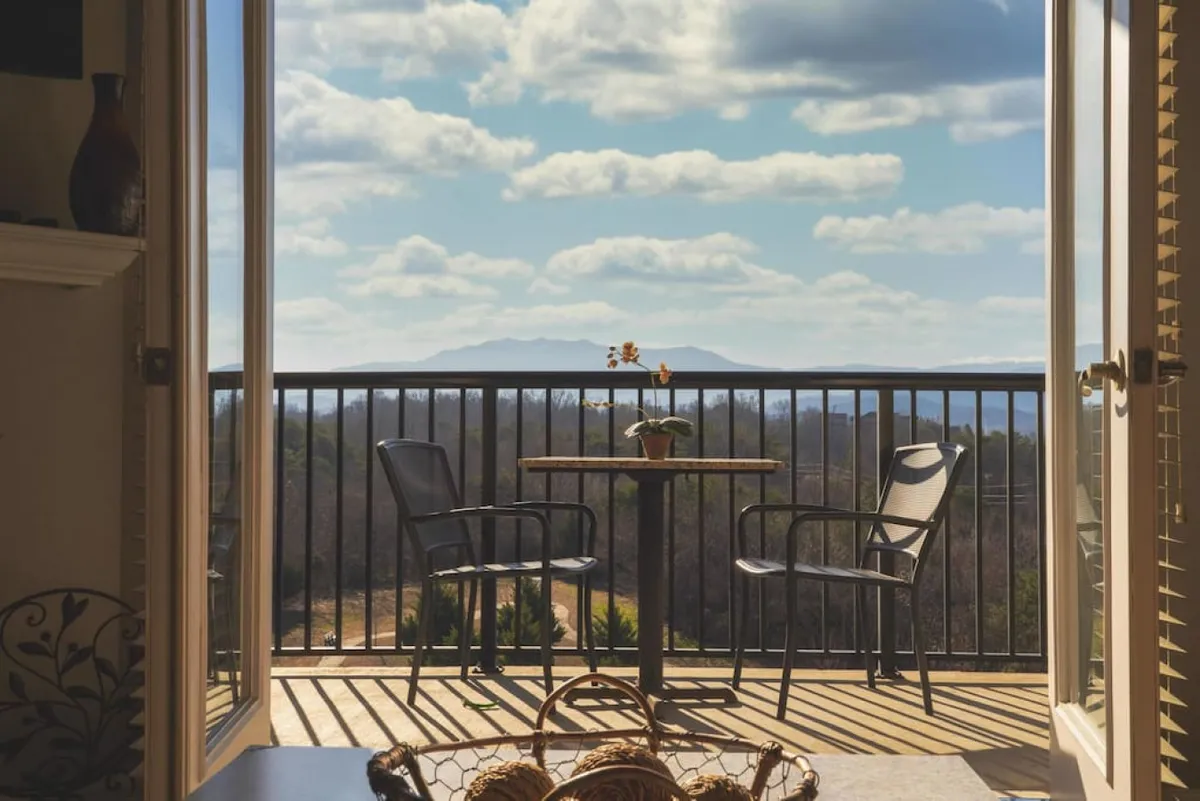 A private balcony with a small table, two chairs, and a flower pot, overlooking a stunning mountain view. The peaceful setting invites guests to enjoy sunrise coffees, quiet conversations, or simply take in the Pigeon Forge mountain scenery.