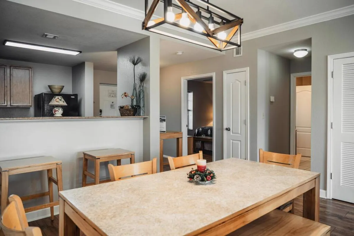 This image presents a spacious dining area centered around a large table with a decorative centerpiece, a stylish lighting fixture, and an open view toward the kitchen. The setup suggests an inviting space for group meals and shared moments.