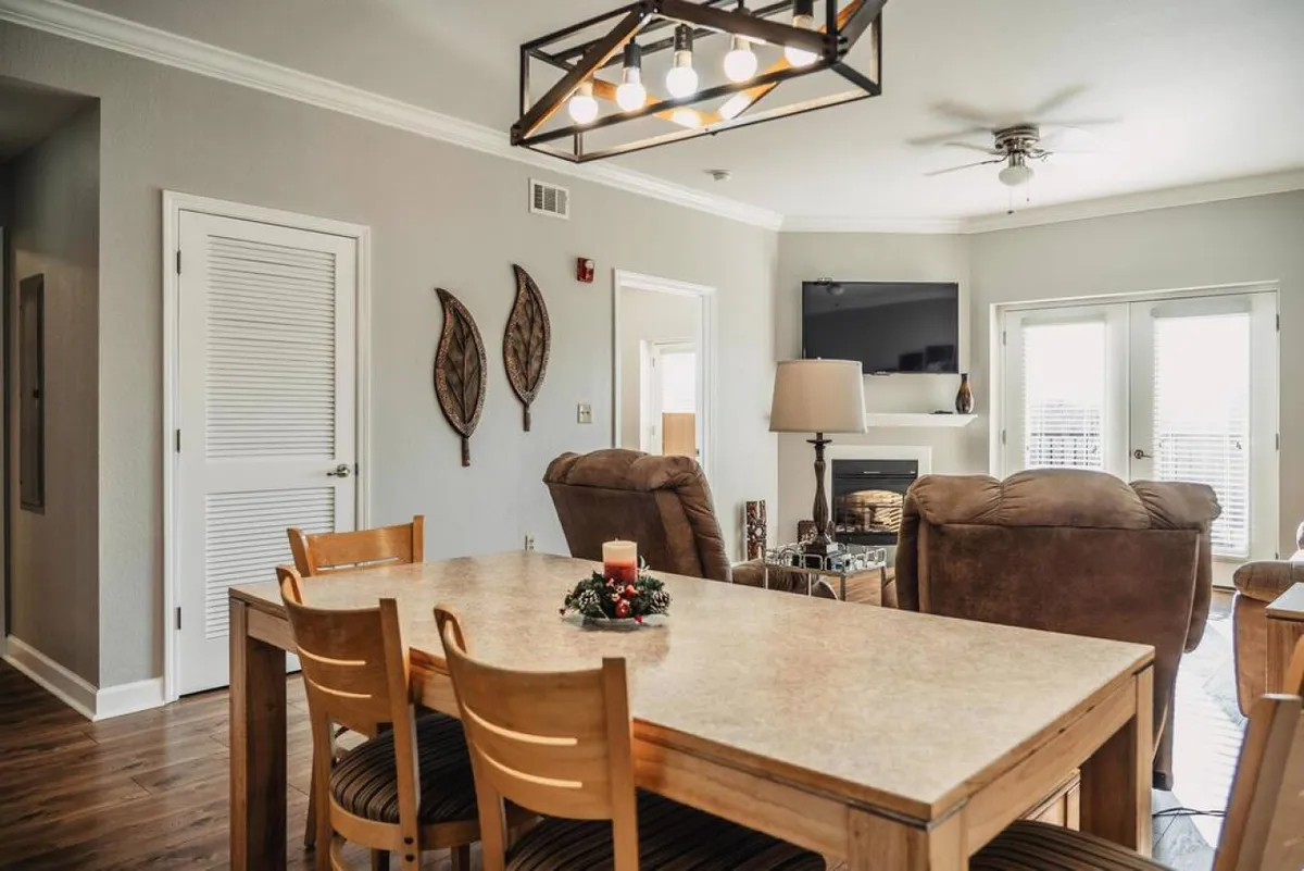 A cozy, welcoming interior scene showcasing a living area with a dining table set for family dinners, a comfortable sofa, a glowing fireplace, and decorative autumn leaves. The mood is festive and warm, perfect for enjoying time indoors during cooler weather.