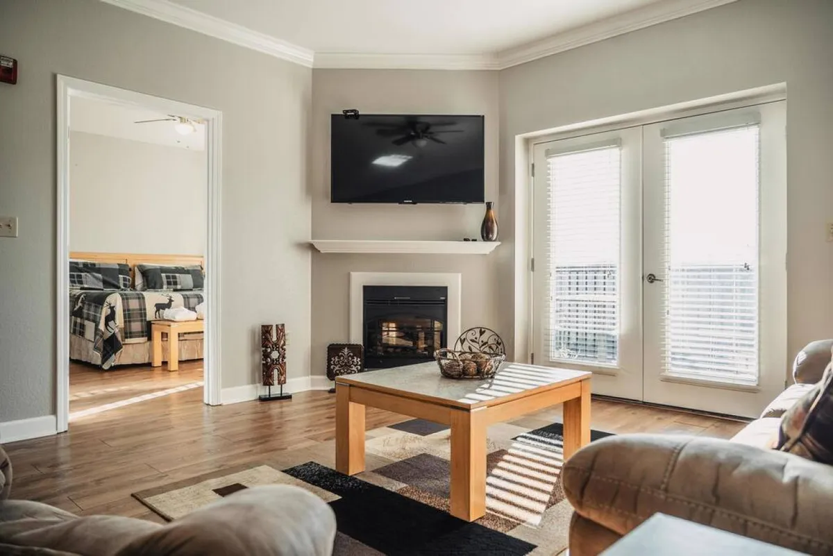 A stylish living area featuring a fireplace, a large television, a spacious coffee table, and sliding doors, with plush furnishings meant for group relaxation. The layout offers ample room for socializing, playing games, or cozy evenings by the fire.