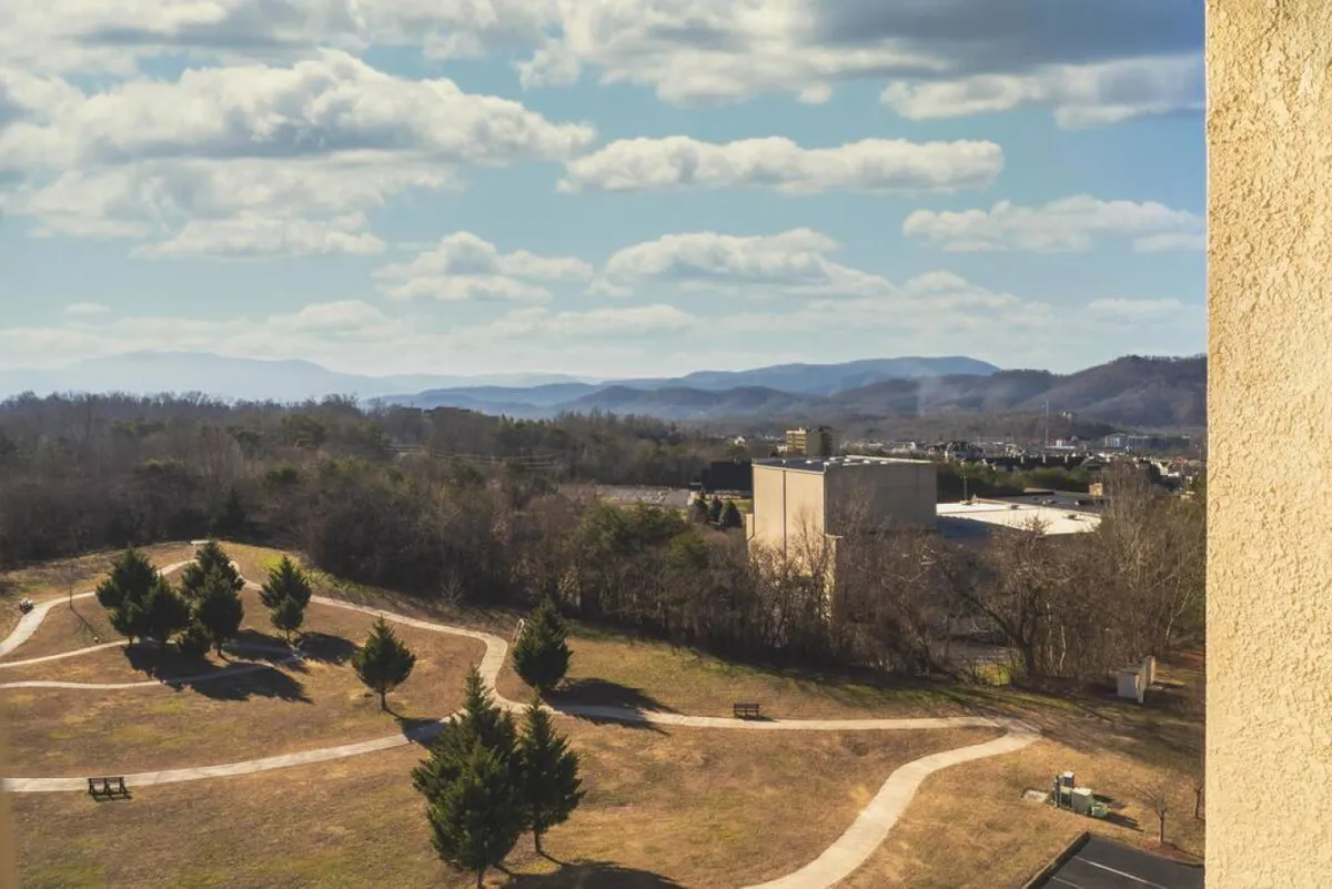 A wide landscape view featuring rolling hills, winding walking paths, scattered trees, and distant mountains. The serene setting invites outdoor activities like walking, picnicking, or simply soaking in natural beauty.
